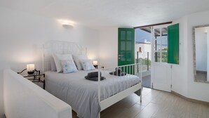 Un dormitorio con cama, mesitas de noche, una puerta verde y vistas a través de una puerta abierta.