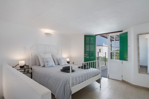 A bedroom with a bed, bedside tables, a green door, and a view through an open door.