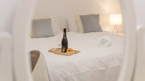 A bed with a tray containing a bottle and glasses, pillows, and a lamp.