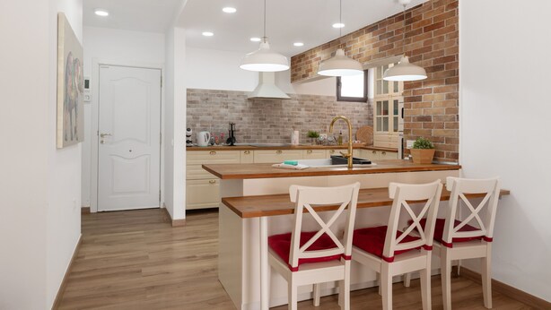 A modern kitchen with a central island, pendant lighting, and a brick accent wall.