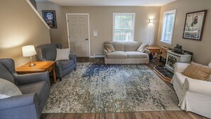 Een woonkamer met een bank, fauteuils, een vloerkleed, een open haard en een trap.