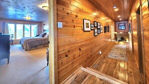 Een houten interieur met een gang die naar een slaapkamer leidt, foto's in lijsten aan de muren en een aan de wand bevestigde televisie.