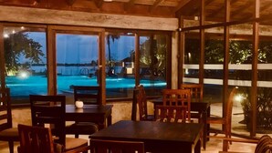 An indoor dining area with wooden tables and chairs, large windows overlooking a swimming pool. - Dinuda Villas Kalpitiya  (Kalpitiya)