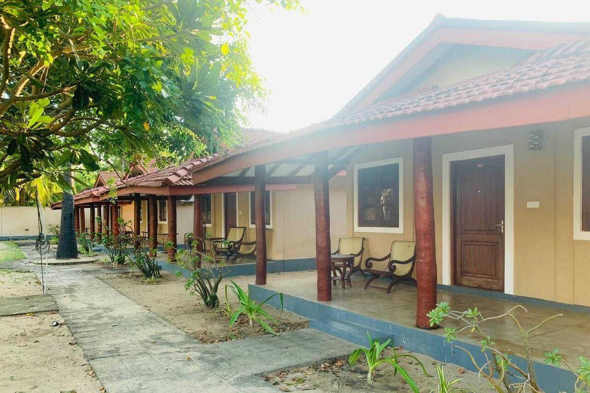 A row of single-story buildings with a covered walkway, outdoor seating, and a palm tree.
