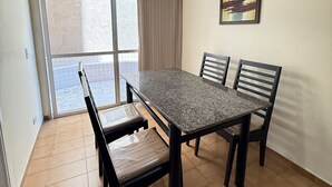 A dining area with a table and chairs, a ceiling fan, a window with curtains, and a painting on the wall. - Pé na Areia Praia do Canto do Forte IV (Praia Grande)