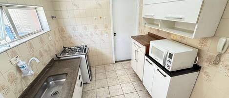A compact kitchen with a gas stove, a microwave, a sink, and a small countertop.