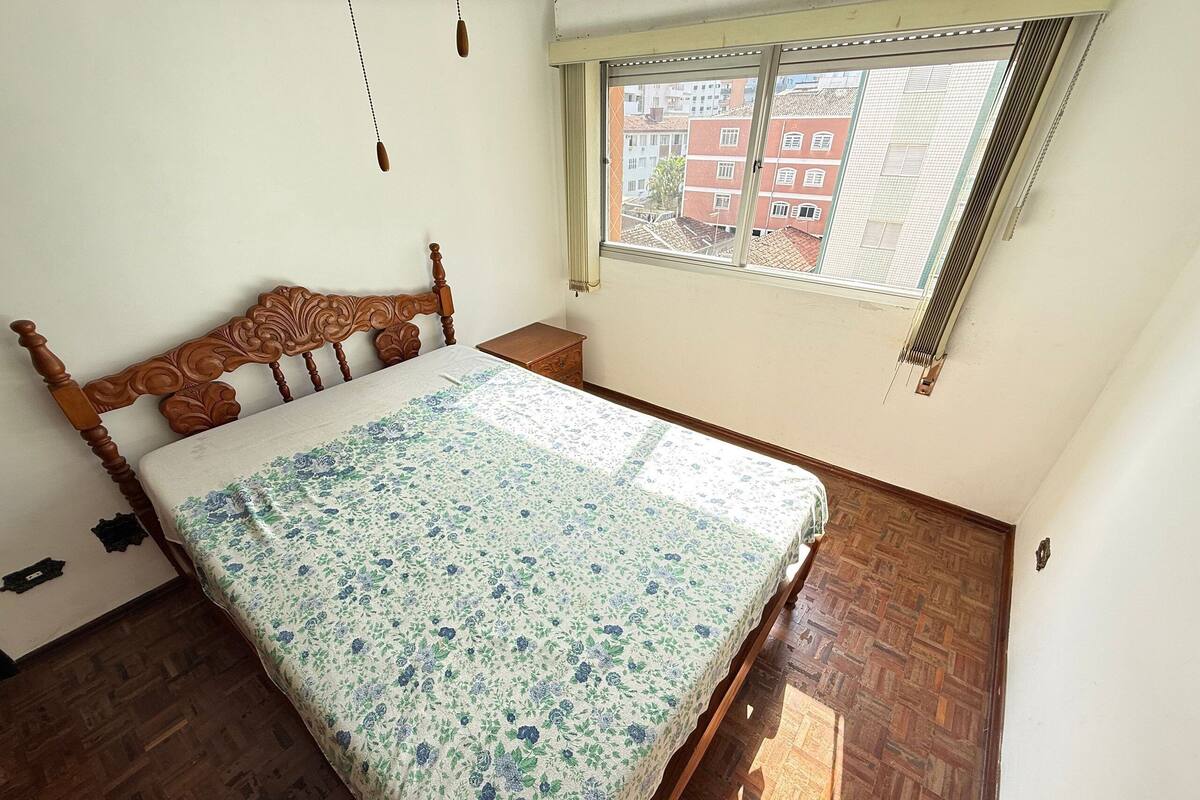 A bedroom with a wooden bed, a window with blinds, and a patterned bedspread.