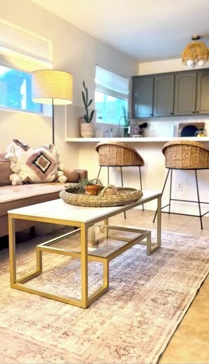 Ein modernes Wohnzimmer mit einem Couchtisch aus Glas, einem gemusterten Teppich und einer Couch mit dekorativen Kissen.
