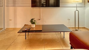 A modern living room with a flat-screen TV mounted on the wall, a coffee table with a plant, a red sofa, and a floor lamp.