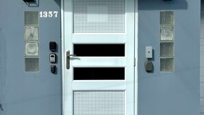 A modern building with a white door, numbered 1357, featuring a keypad lock, a peephole, and a small window above the door.