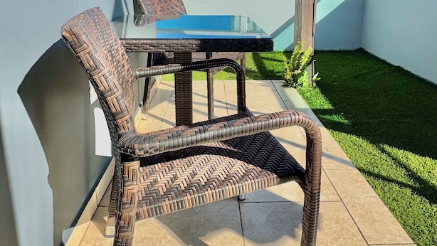 A patio with a glass table and wicker chairs, a small lawn, and a view of buildings in the background.