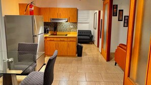 A modern kitchen with wooden cabinets, a refrigerator, and a microwave. There is a dining area with a glass table and chairs.