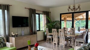 Ein geräumiger Wohnbereich mit Deckenventilator, Fernseher, Esstisch mit Stühlen und einer Couch mit grünen Kissen.