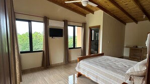 Ein geräumiges Schlafzimmer mit einem großen Bett, Holzbalken an der Decke, einem Deckenventilator und einem an der Wand montierten Fernseher.