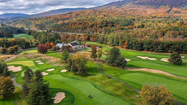 Ein Golfplatz mit Clubhaus, umgeben von herbstlich gefärbten Bäumen und Hügeln.
