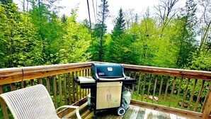 Eine Holzterrasse mit Grill, gepolstertem Stuhl und Blick auf einen Wald.