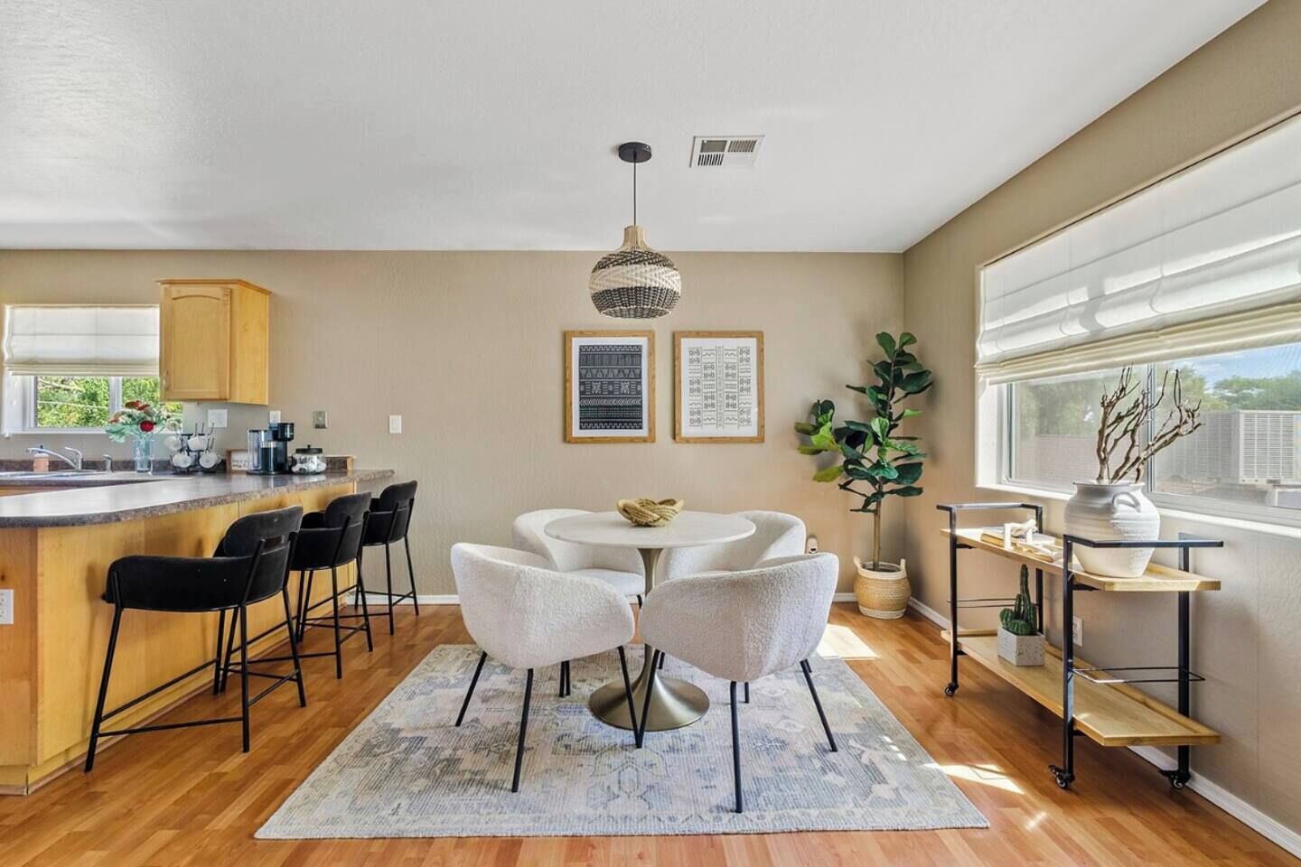 Una cocina moderna con una isla central, taburetes de bar, una mesa de comedor redonda con sillas, una lámpara colgante y un ventanal con vistas.