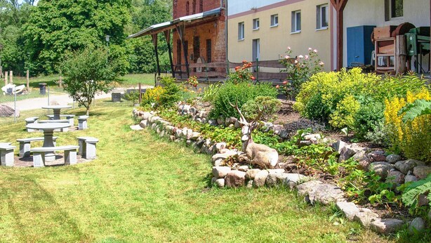 Un jardín con un ciervo, mesas de picnic y un edificio de fachada de ladrillo.