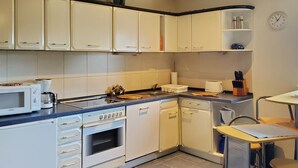 Una cocina compacta con armarios blancos, un microondas Bosch, un tostador y un lavamanos.
