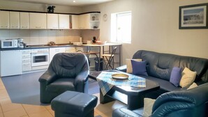 Un espacio habitable compacto con kitchenette, comedor y zona de estar con sofá y sillas.