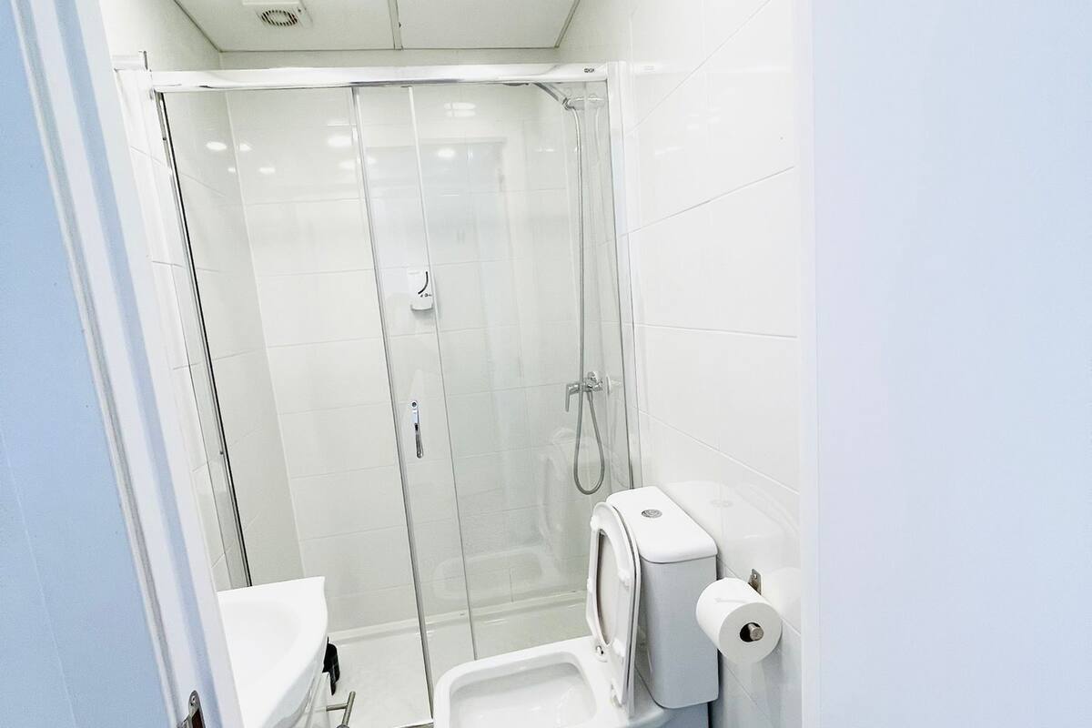 Een kleine badkamer met een douche, toilet en een blauwe wasmand.