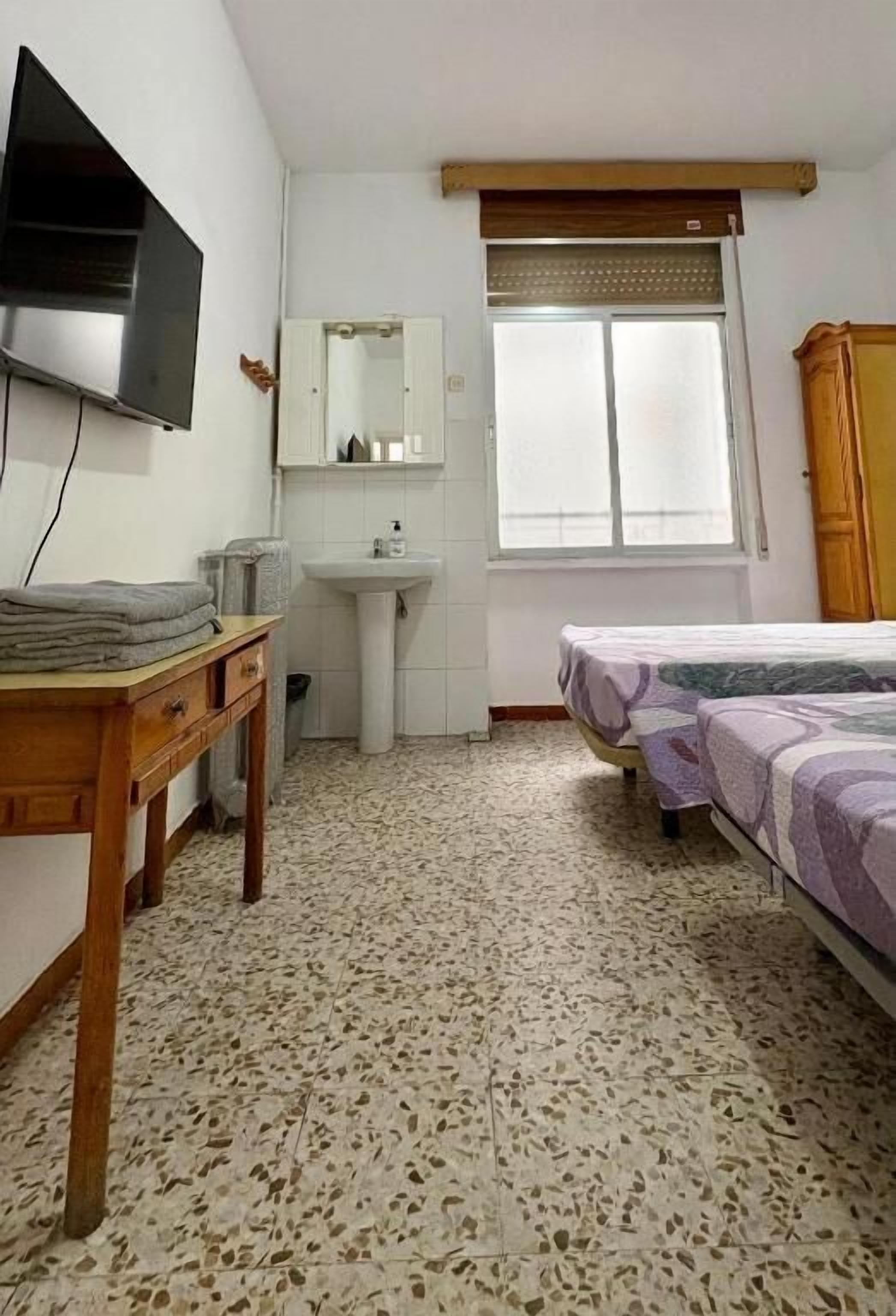 A bedroom with a bed, a television, a sink, and a window.