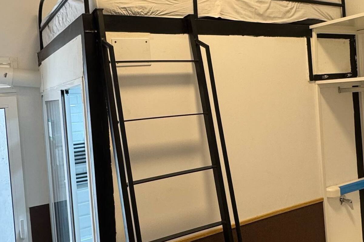 Een stapelbed met een ladder, een klein raam en een witte deur.