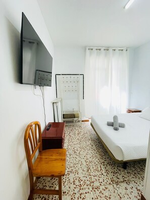 Une chambre d’hôtel avec un lit, un téléviseur fixé au mur, une chaise en bois, une petite table et un radiateur.