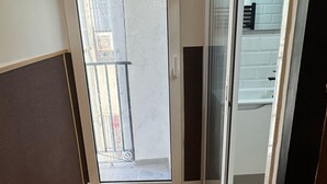 A room with a wooden floor, a sliding glass door leading to a balcony, and a view of a building outside. - Hostal Ruano (Madrid)