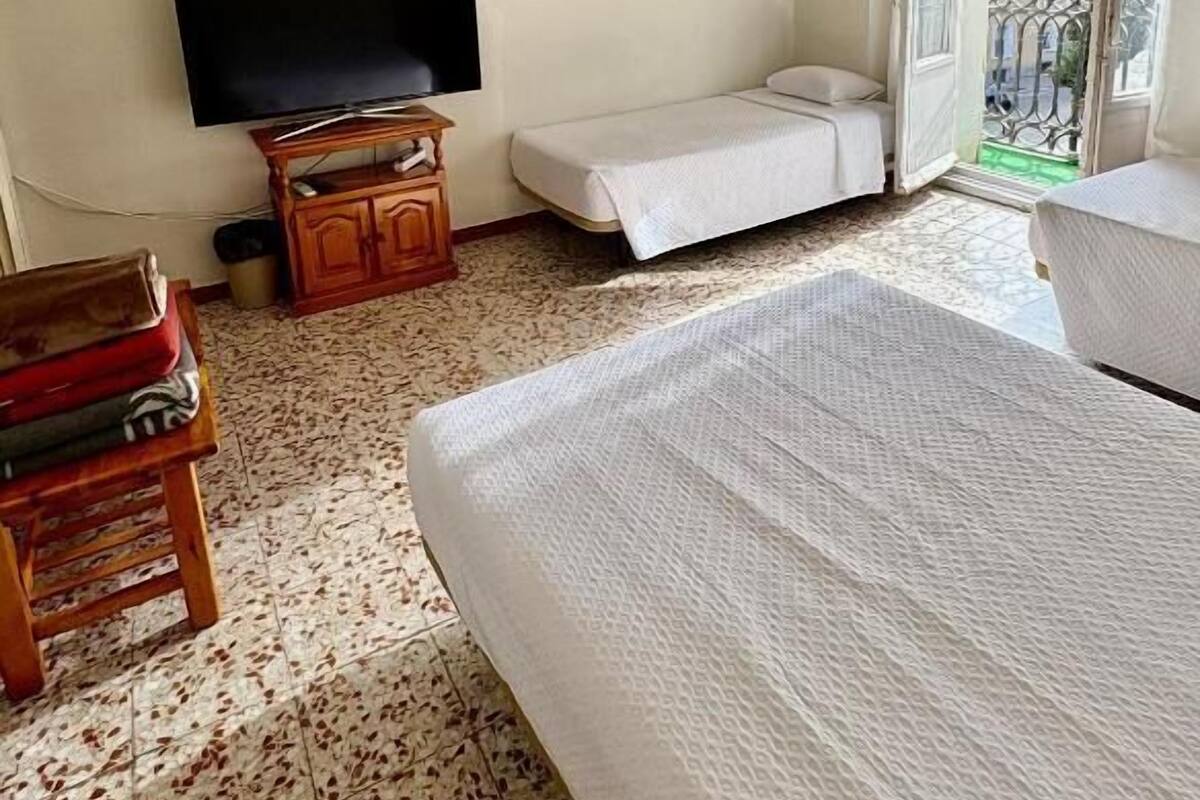 Een kamer met een bed, een televisie, een klein houten kastje en een bankje.