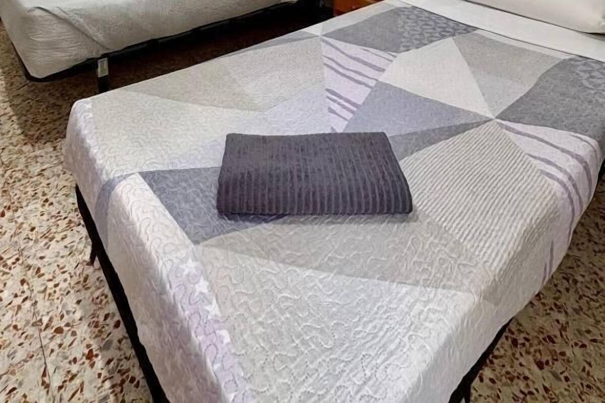 Een kamer met twee enkele bedden, een klein houten nachtkastje en een kamerbreed tapijt met dessin.