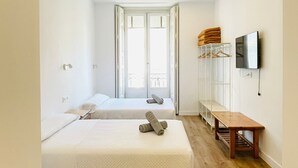 A hotel room with two beds, a wooden floor, a TV mounted on the wall, and a window with a view. - Hostal Ruano (Madrid)