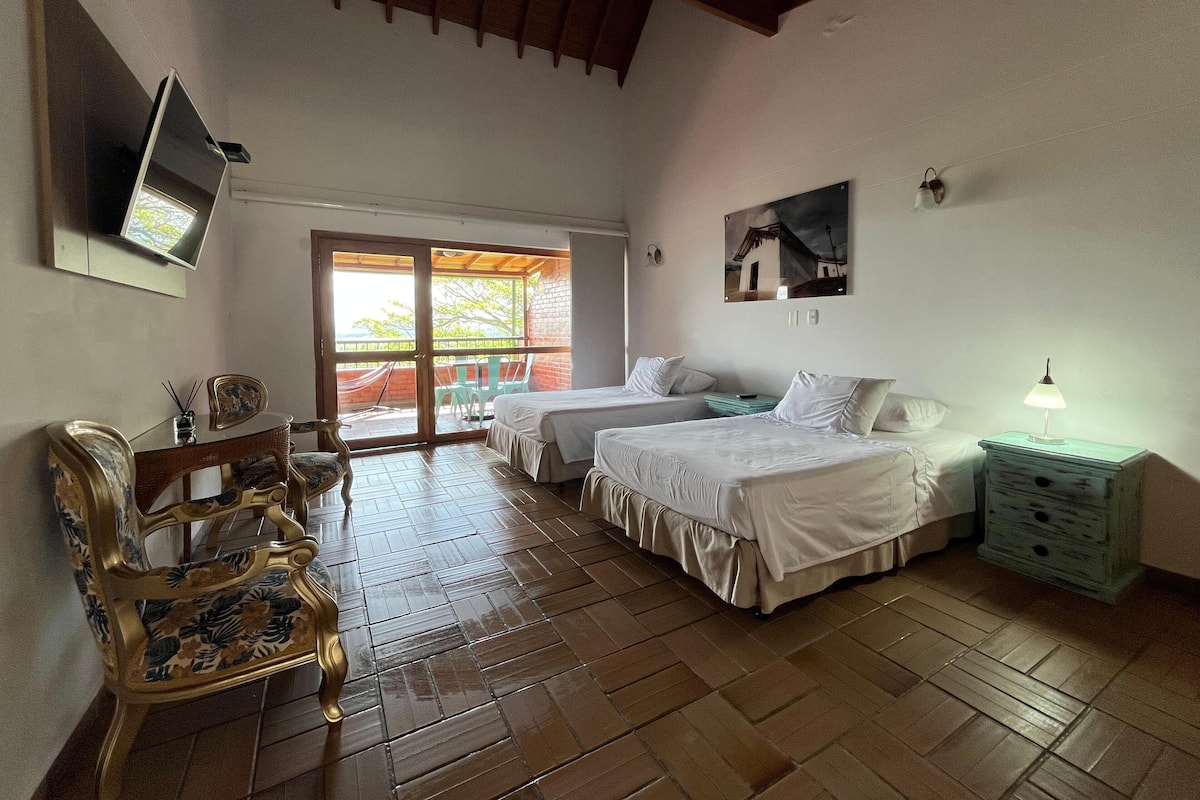 Une chambre avec deux lits, un plafond en bois, un téléviseur fixé au mur et un balcon avec des chaises.