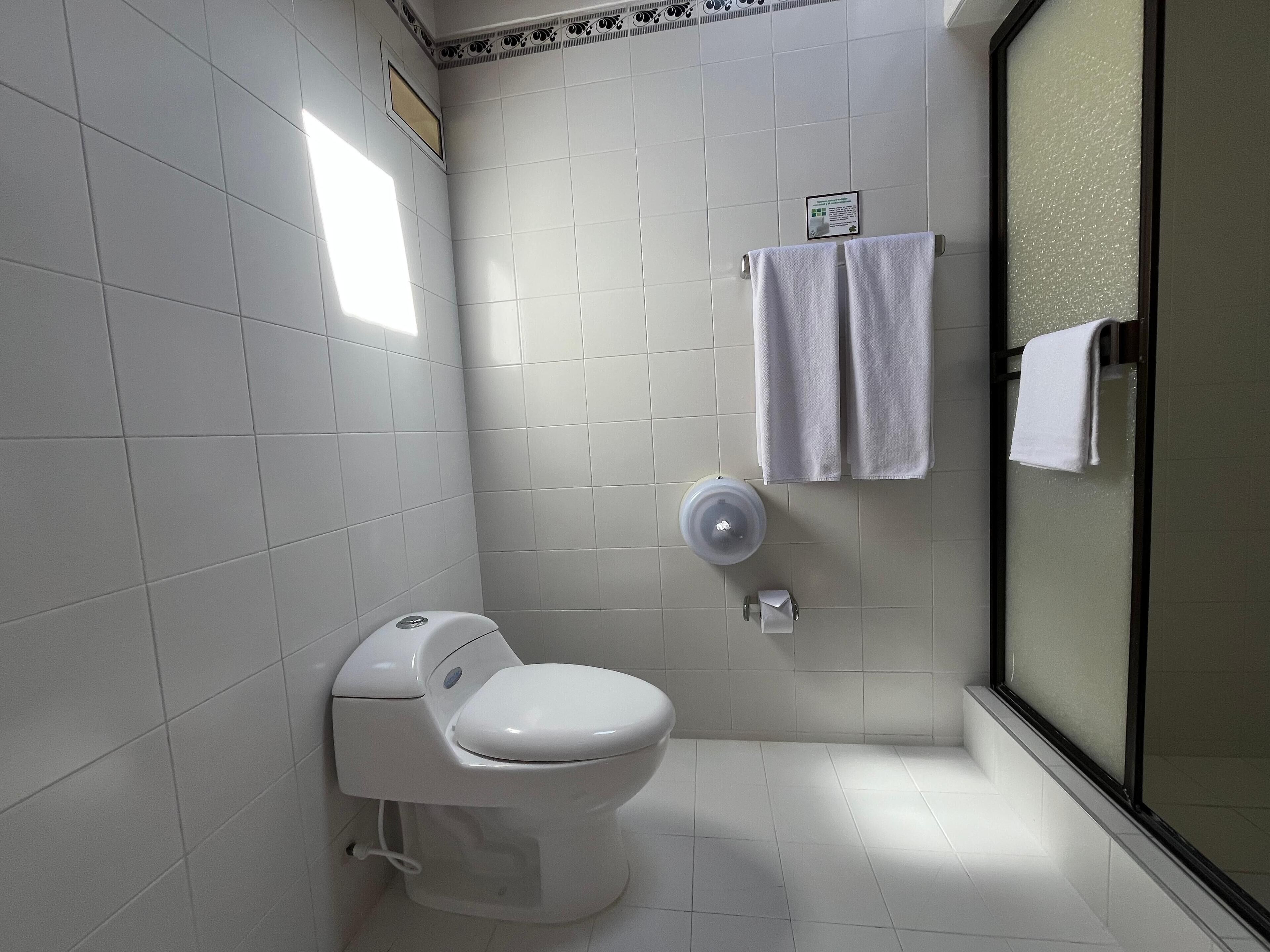 A modern bathroom with a toilet, a hand dryer, and a glass shower enclosure.