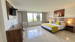 Una camera d'albergo con un letto, comodini, una scrivania, una sedia, una TV fissata al muro e una finestra vista verde.
