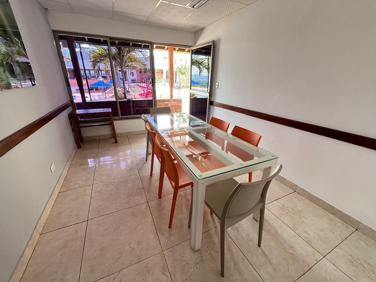 Un salón de conferencias con una mesa y sillas de vidrio, amplias ventanas que dan a un patio al aire libre.