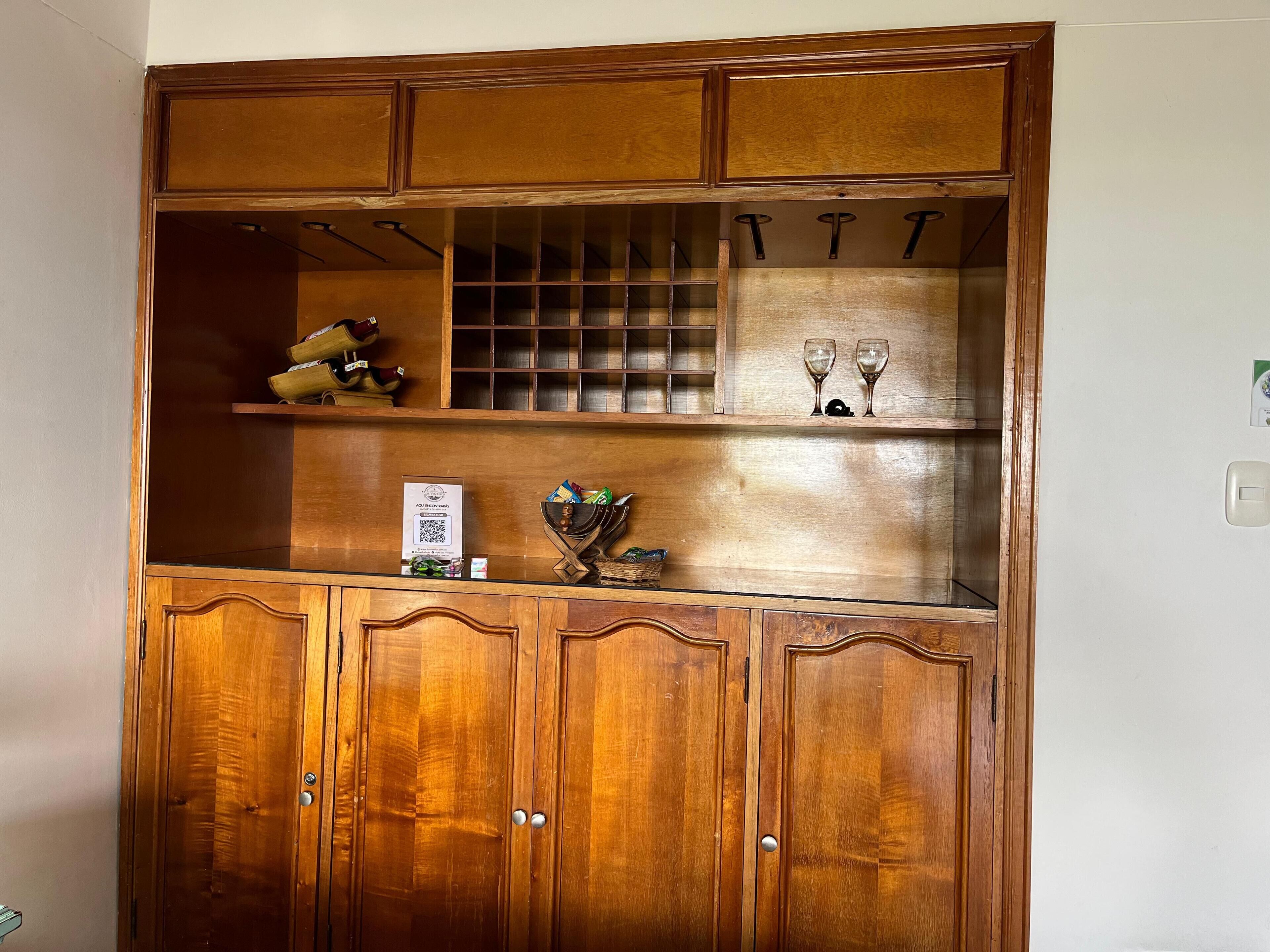 A wooden cabinet with multiple compartments, including shelves for shoes and wine glasses, and a section with a QR code.