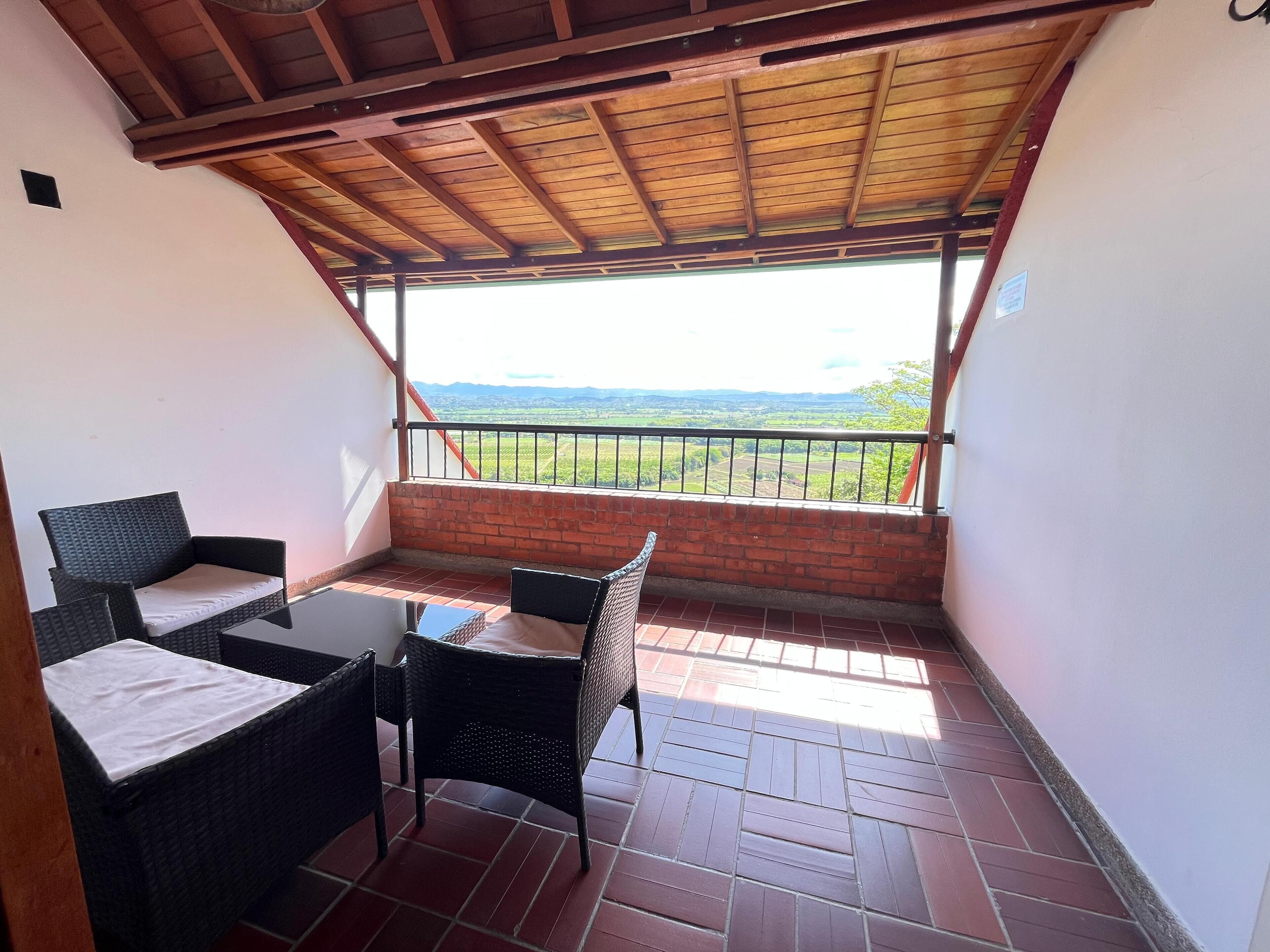 A balcony with wicker furniture, a brick wall, and a view of distant fields.