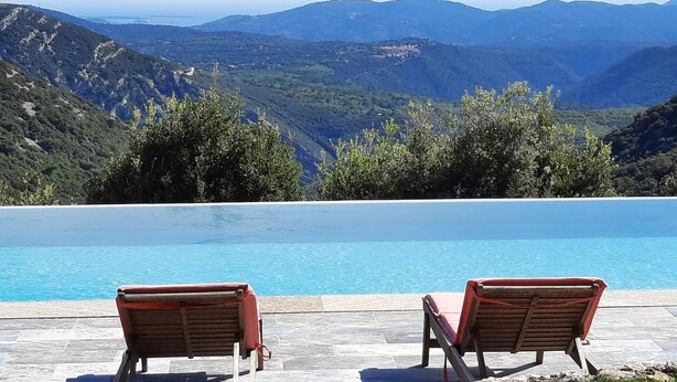 A poolside area with two wooden lounge chairs and a view of a mountainous landscape. - Mas des Louquiers (MONS)