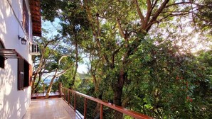 Un balcon doté d’un sol carrelé, d’une balustrade en bois et offrant une vue sur un feuillage dense et des arbres.