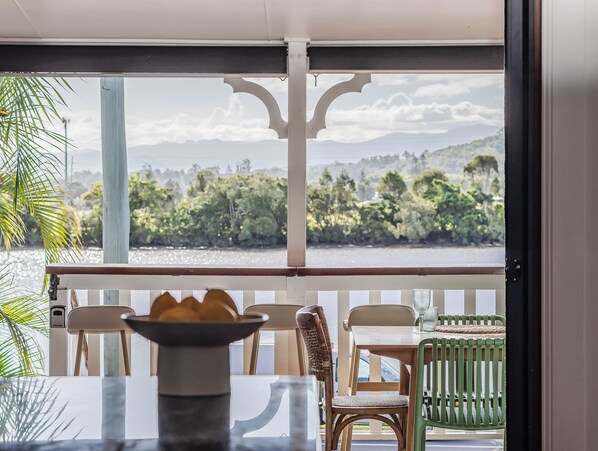 A room with a view of a body of water and greenery, a table with chairs, and a decorative vase. - Riviera Palms (Tumbulgum)
