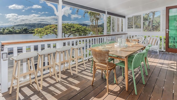 Un espace extérieur abrité doté d ’une terrasse en bois, de rampes blanches et d’une table dressée pour le repas.