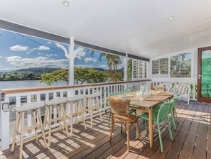 A covered outdoor area with a wooden deck, white railings, and a table set for dining. - Riviera Palms (Tumbulgum)
