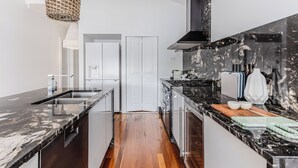 Une cuisine moderne dotée d’un plan de travail en marbre, d’appareils électroménagers en acier inoxydable et d’un plancher en bois.