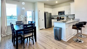 A modern kitchen with white cabinets, stainless steel appliances, and a dining area with a wooden table and chairs. - 🤍Modern Alamo City Retreat🤍 (San Antonio)