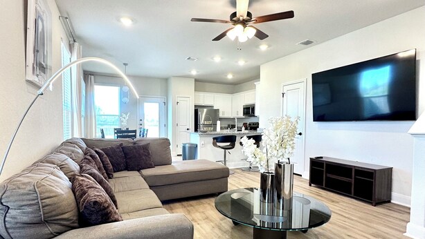 A modern living room with a sectional sofa, a glass coffee table, and a flat-screen TV. - 🤍Modern Alamo City Retreat🤍 (San Antonio)