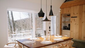 Comedor con mesa de madera dispuesta para cuatro personas, rodeado de sillas de mimbre, con lámparas colgantes arriba.