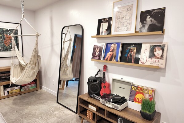 A room with a hammock, a mirror, a shelf with framed pictures, a record player, and a small plant.