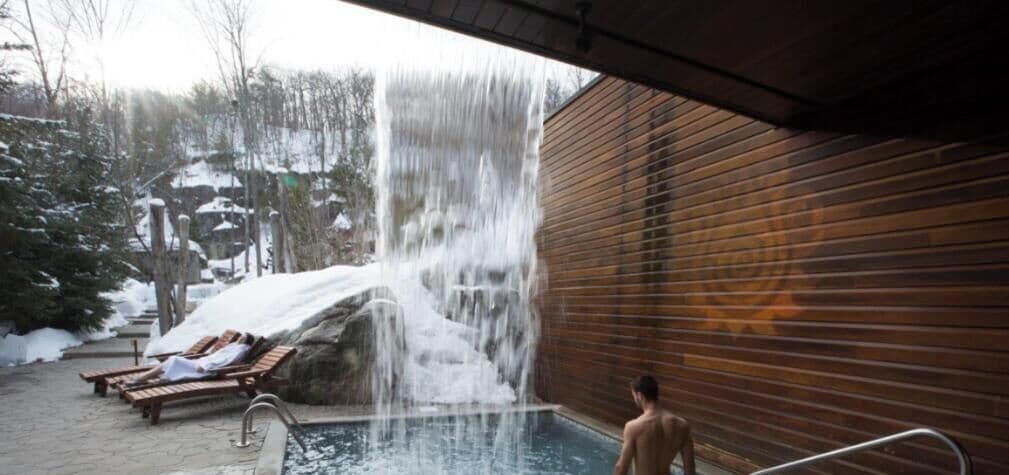 Une piscine agrémentée d’une cascade, des chaises longues en bois et un mur en bois.
