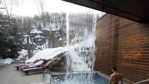 Una piscina con una cascada, sillones de madera y un muro de madera.